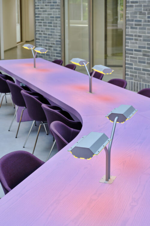 Purple linoil table in shape of train tracks with industrial reading lights in coworking space design object by dutch invertuals studio