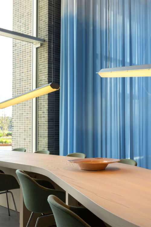 wooden work table with curved shape with industrial hanging lights and blue cloud curtain in coworking space in Breda design objects by dutch invertuals studio